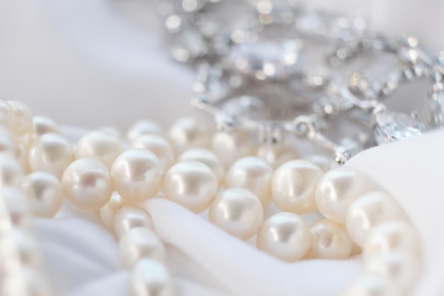 Un primer plano de un collar de perlas con un colgante de diamantes brillantes en un fondo de tela blanca esta imagen