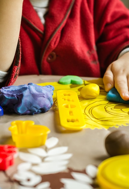 Foto primer plano de coloridos moldes de plastilina y manos de niños jugando en el fondo