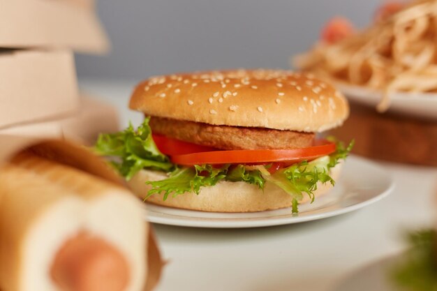 Primer plano de comida chatarra en la mesa sabrosa salchicha en masa hamburguesa grande y pasta con tomates Comida callejera hamburguesas de chuleta de carne Entrega de alimentos