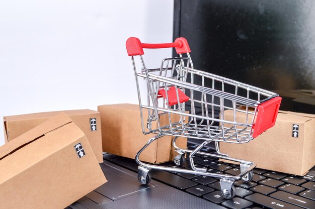 Un primer plano de una computadora portátil con un carrito de compras y cajas de cartón sobre un fondo blanco
