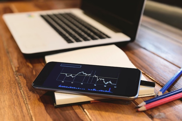 Foto primer plano de la computadora portátil con gráfico mostrado en la pantalla del teléfono inteligente en la mesa