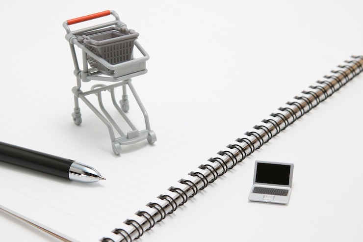 Foto primer plano de una computadora portátil de juguete con un carrito de compras y un cuaderno en espiral contra un fondo blanco