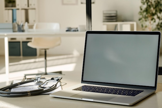 Primer plano de una computadora portátil con pantalla vacía en el lugar de trabajo del médico en la oficina