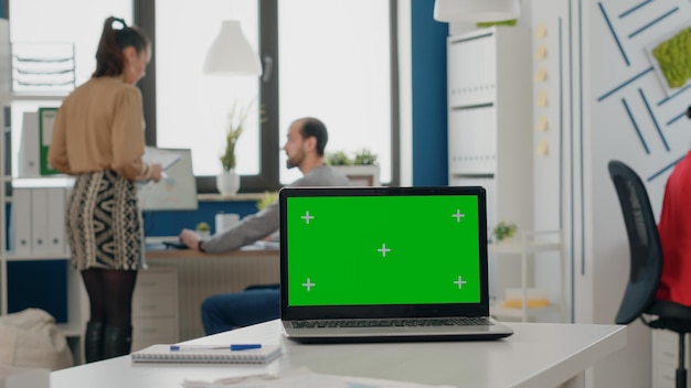 Primer plano de la computadora portátil con pantalla verde en el escritorio vacío en la oficina comercial. Plantilla simulada con fondo de clave de croma aislado en la computadora en el espacio de inicio. Espacio de copia de maqueta en exhibición