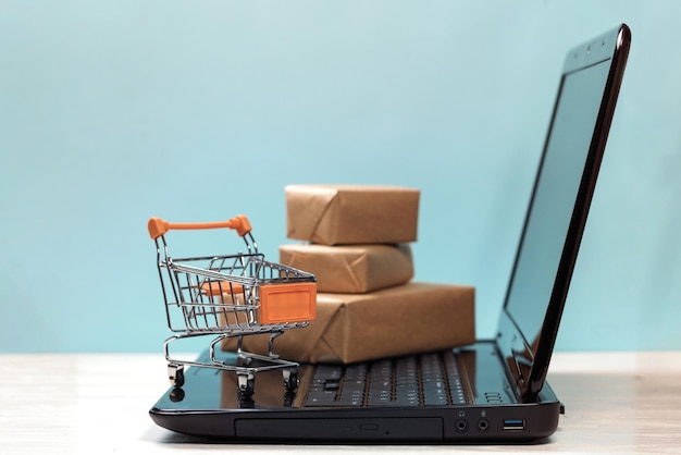 Primer plano de una computadora portátil con paquetes y carrito de compras en la mesa contra la pared