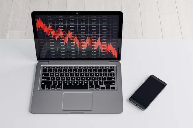 Primer plano de la computadora portátil y el teléfono celular en el escritorio con la caída de la cuadrícula de gráficos de negocios rojos sobre fondo borroso Recesión de crisis y concepto de mercado de valores Representación 3D