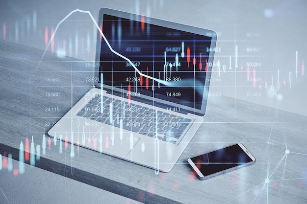 Primer plano de la computadora portátil y el teléfono inteligente en el escritorio de madera con gráfico de forex de velas brillantes y holograma de mapa sobre fondo borroso Mercado de inversión bursátil y concepto de dinero Doble exposición