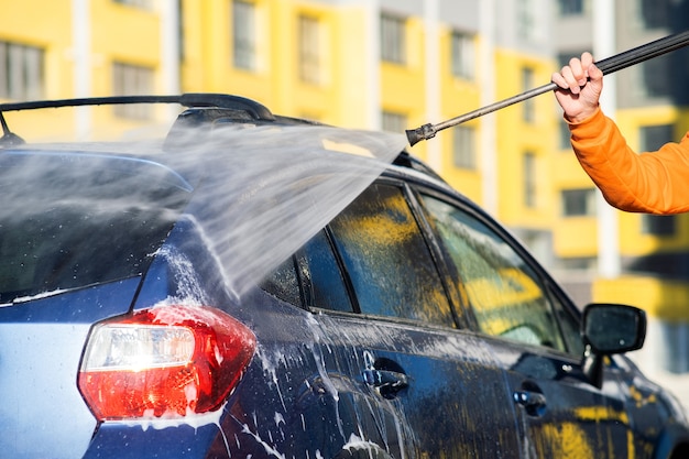 Primer plano de un conductor masculino lavando su coche con chorro de agua a alta presión sin contacto