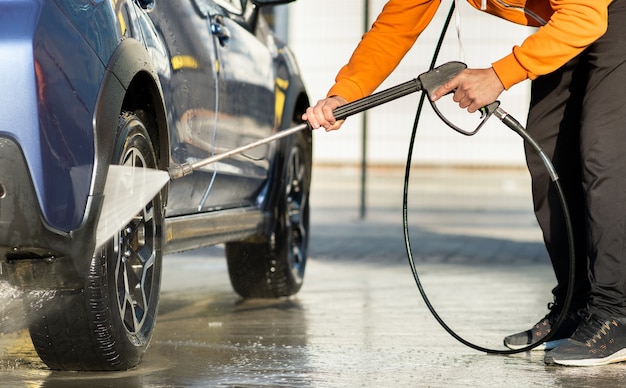 Primer plano de un conductor masculino que lava su automóvil con un chorro de agua a alta presión sin contacto en un autoservicio de lavado de automóviles.