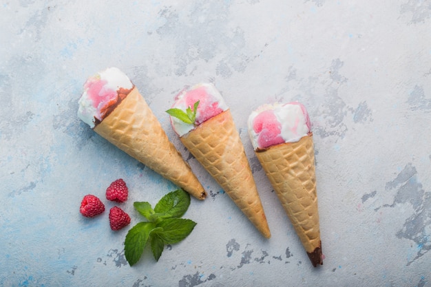 Primer plano de cono de helado. Cucharada rosada del helado en cono de la galleta sobre fondo concreto. aplanada, a la vista. Sabor a fresa o frambuesa. Postre dulce closeup