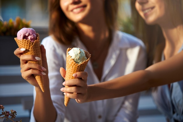 Primer plano de conos de helado en la mano de una mujer de pie con su amiga dos mujeres jóvenes