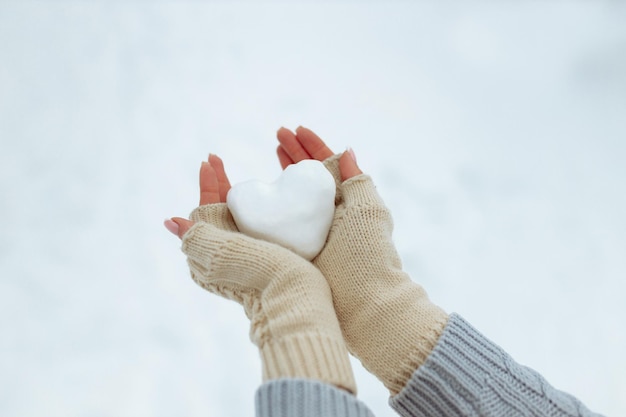 Primer plano Corazón de nieve en manos con guantes de punto en el fondo de la cubierta de nieve Día de San Valentín