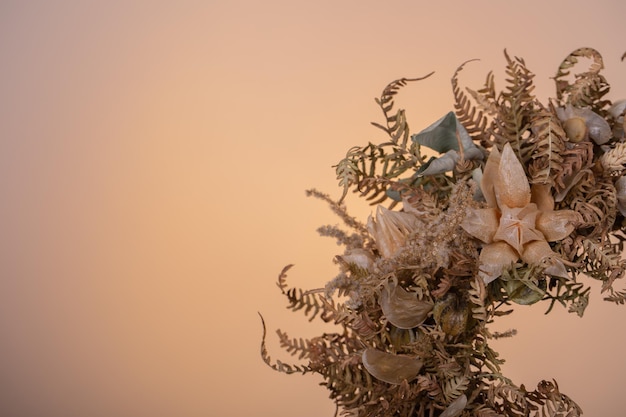 primer plano de una corona de flores secas con physalis y helecho en un fondo de melocotón