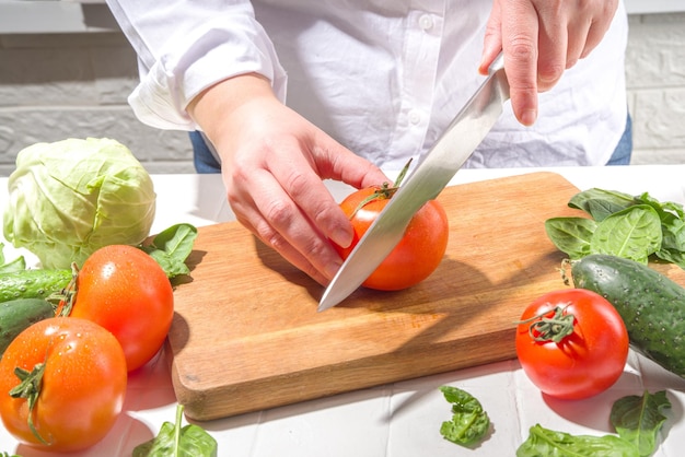 Primer plano de cortar rodajas de tomates frescos Manos de mujer cortadas con cuchillo verduras de tomate fresco