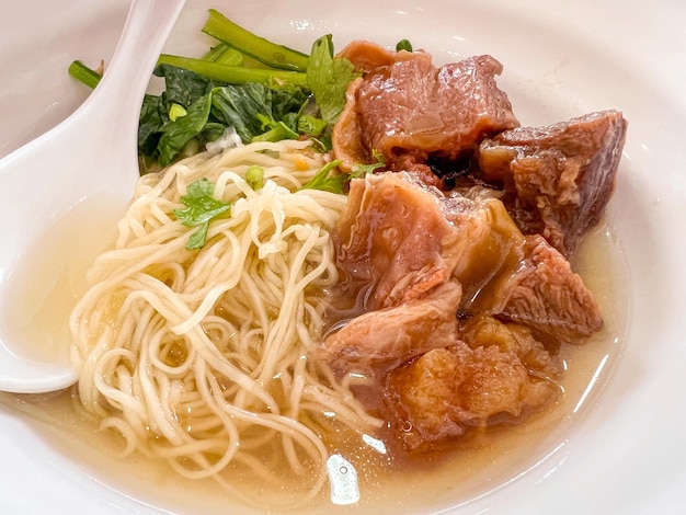 Primer plano y cosecha de fideos de huevos chinos con sopa de carne guisada en un tazón de cerámica blanca