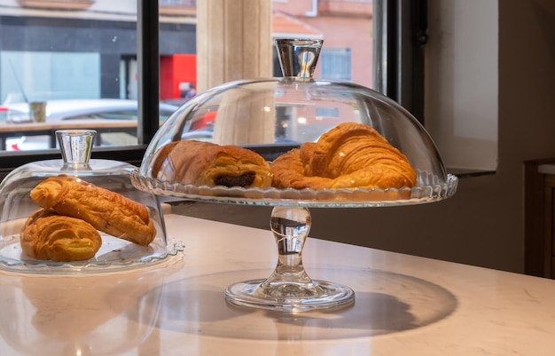 Primer plano de un croissant casero apetitoso o cruasan en un vaso de vidrio en el mostrador de una pastelería o cafetería.