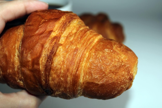 Primer plano de croissant crujiente fresco en la mano Fondo claro borroso Cocinar hornear en casa