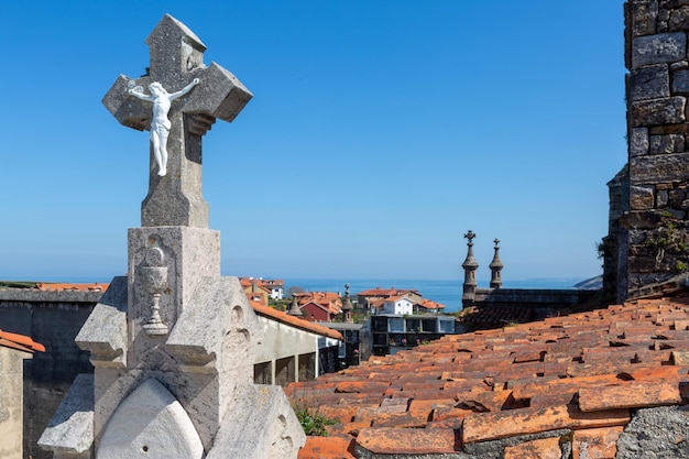 Primer plano de una cruz de piedra con la figura de Jesucristo en el cementerio con vistas al mar