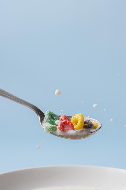 Primer plano de una cuchara con leche y cereales coloridos en forma de anillo Gotas de leche cayendo