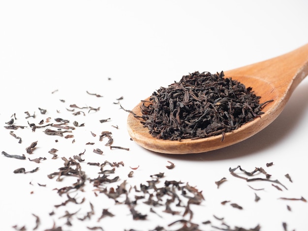 Foto primer plano de una cuchara de madera con negro que en un fondo blanco hojas de té están esparcidas alrededor