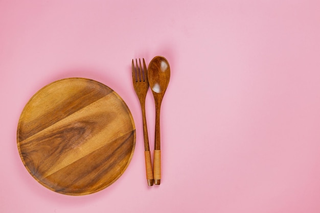 Primer plano de cuchara y tenedor de plato de madera sobre fondo rosa