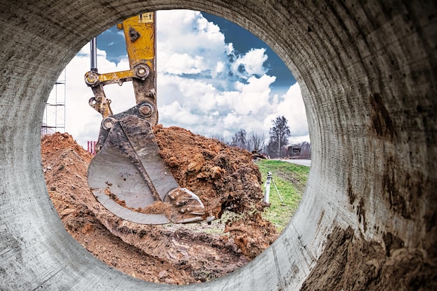 El primer plano del cucharón de la excavadora contra el cielo azul excava el movimiento de tierras del suelo con equipo pesado en el sitio de construcción