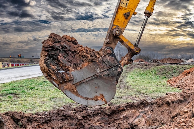 Primer plano del cucharón de la excavadora en el sitio de construcción La excavadora está cavando una zanja para servicios subterráneos Equipos de construcción para movimiento de tierras