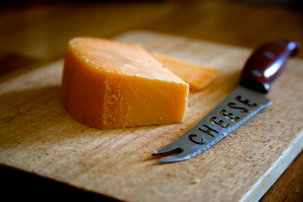 Primer plano de un cuchillo con queso en la tabla de cortar en la mesa