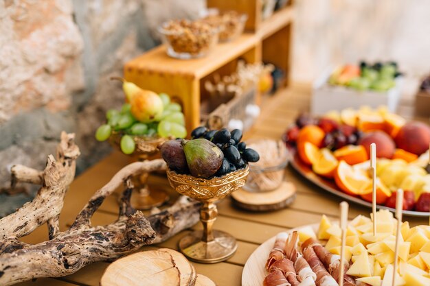 Primer plano de un cuenco dorado de uvas e higos sobre una mesa con lonchas de jamón, queso y fruta en placas