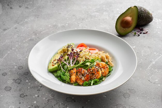 Primer plano, cuenco con langostinos tigre, quinoa y aguacate y aceite de oliva sobre piedra gris