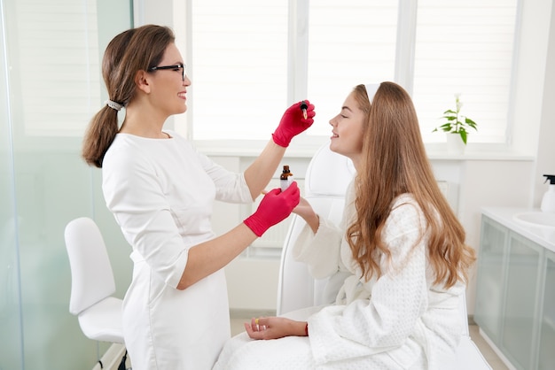 Primer plano del cuidado de la piel de la cara de la hermosa mujer sonriente que recibe el tratamiento con aceite de suero en un salón de belleza