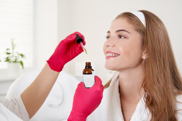 Primer plano del cuidado de la piel de la cara de la hermosa mujer sonriente que recibe el tratamiento con aceite de suero en un salón de belleza