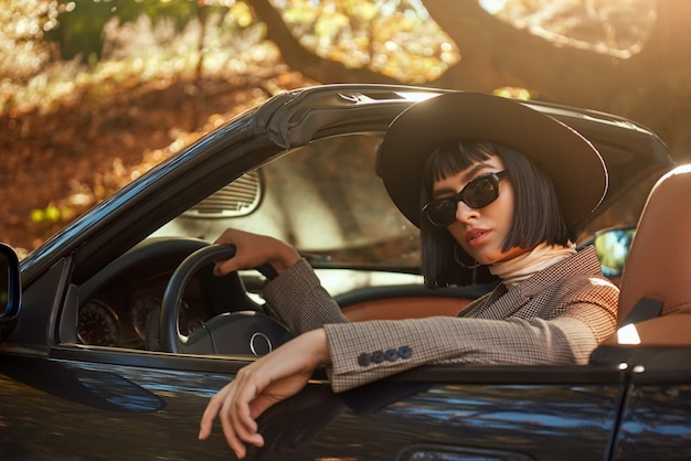 Primer plano de una dama sexy con gafas de sol y sombrero está sentado en cabriolet