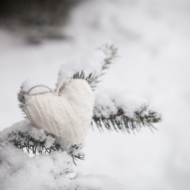 Primer plano de la decoración navideña de corazón tejido en el árbol de Navidad con nieve al aire libre