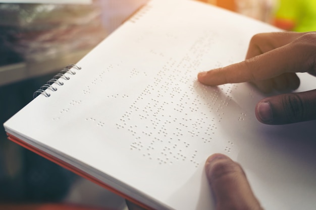 Foto primer plano de los dedos leyendo braille, mano de una persona ciega leyendo algunos textos en braille de un libro en braille.