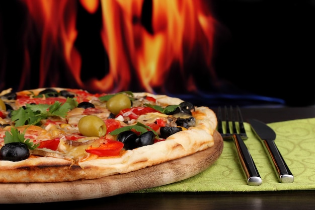 Primer plano de deliciosa pizza en la mesa de madera sobre fondo de fuego