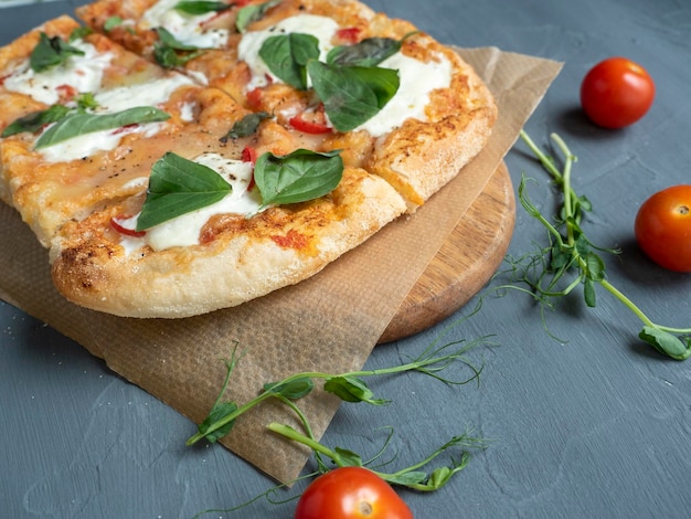 Primer plano de una deliciosa pizza romana fresca y crujiente con queso y hierbas sobre un fondo gris Los tomates maduros frescos están cerca Papel artesanal Vista lateral Enfoque selectivo