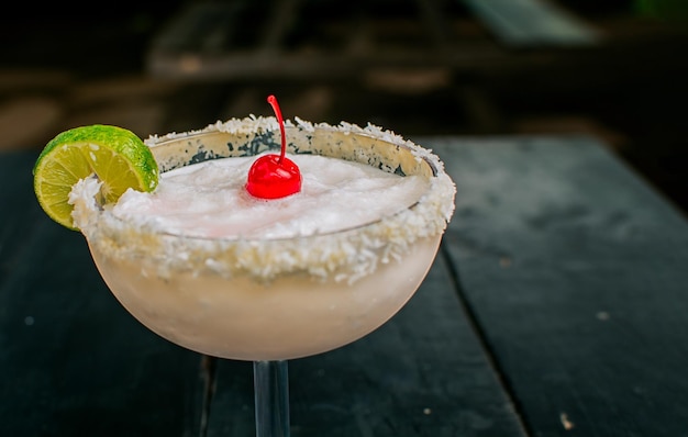 Primer plano de un delicioso cóctel de coco congelado con cereza Margarita de coco congelado con rebanada de limón servida en una mesa de madera