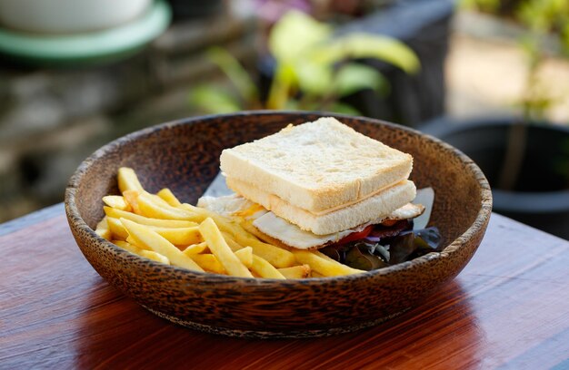 Primer plano delicioso sabroso delicioso desayuno casero huevo frito tocino de cerdo y sándwich de queso pan de vanguardia con corte recto freír papas fritas frescas aperitivo en un tazón de madera en la mesa de madera