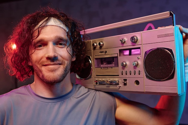 Primer plano de un deportista caucásico sonriente posando con una grabadora retro estética de fitness retro