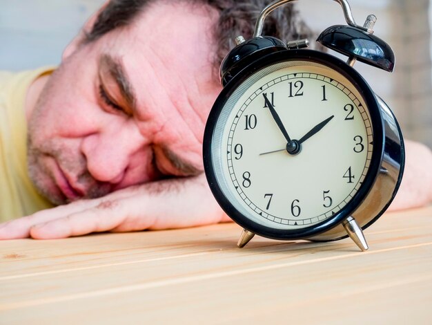 Primer plano del despertador por un hombre durmiendo en la mesa