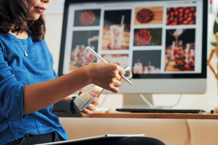Foto primer plano del diseñador asiático serio con lápiz sentado contra el monitor de la computadora y elegir el color en la muestra de color
