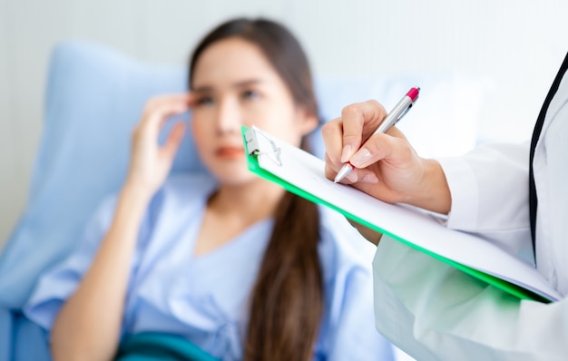 Primer plano de la doctora asiática joven asesoría terapéutica con emociones positivas para el paciente femenino joven asiático en cama en el hospital.