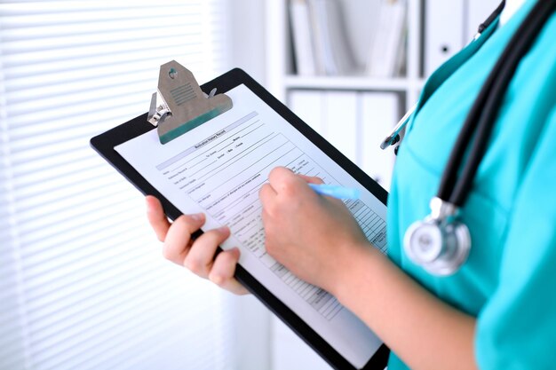 El primer plano de una doctora está llenando el formulario de solicitud o el historial médico