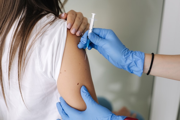 Primer plano de una doctora en guantes protectores sosteniendo una jeringa haciendo que las mujeres de vacunación covid obtengan