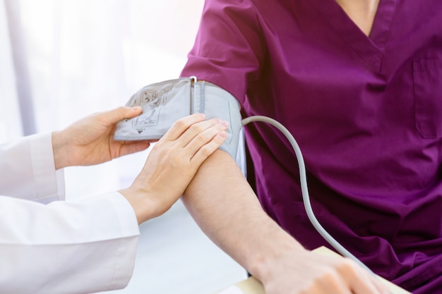 Primer plano de la doctora con la medición de la presión en el brazo de un paciente masculino use el brazo con un medidor de presión digital para una mejor curación en la sala del hospital.