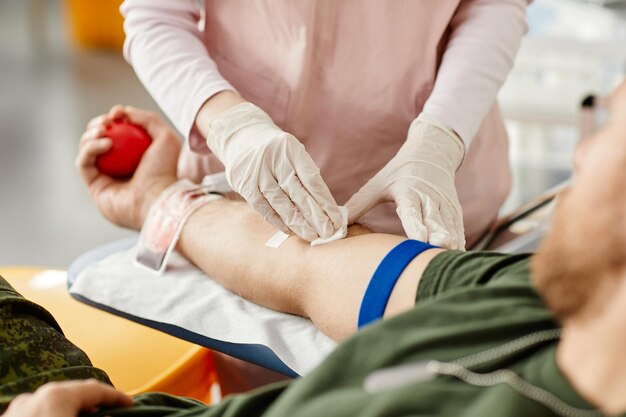 Primer plano de un donante masculino que dona sangre en el centro de donación con una enfermera que ayuda a copiar el espacio