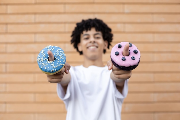 Primer plano de un donut morado con arándanos glaseados y un donut azul con cuentas en los dedos