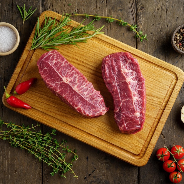 Primer plano de dos bistec de carne cruda de hoja superior sobre tabla de madera con especias y hierbas