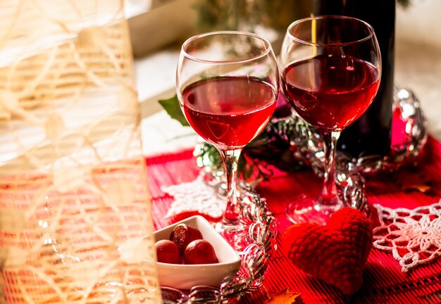 primer plano dos copas de vino tinto en la mesa de Año Nuevo decorada festivamente en el fondo de la ventana de luz